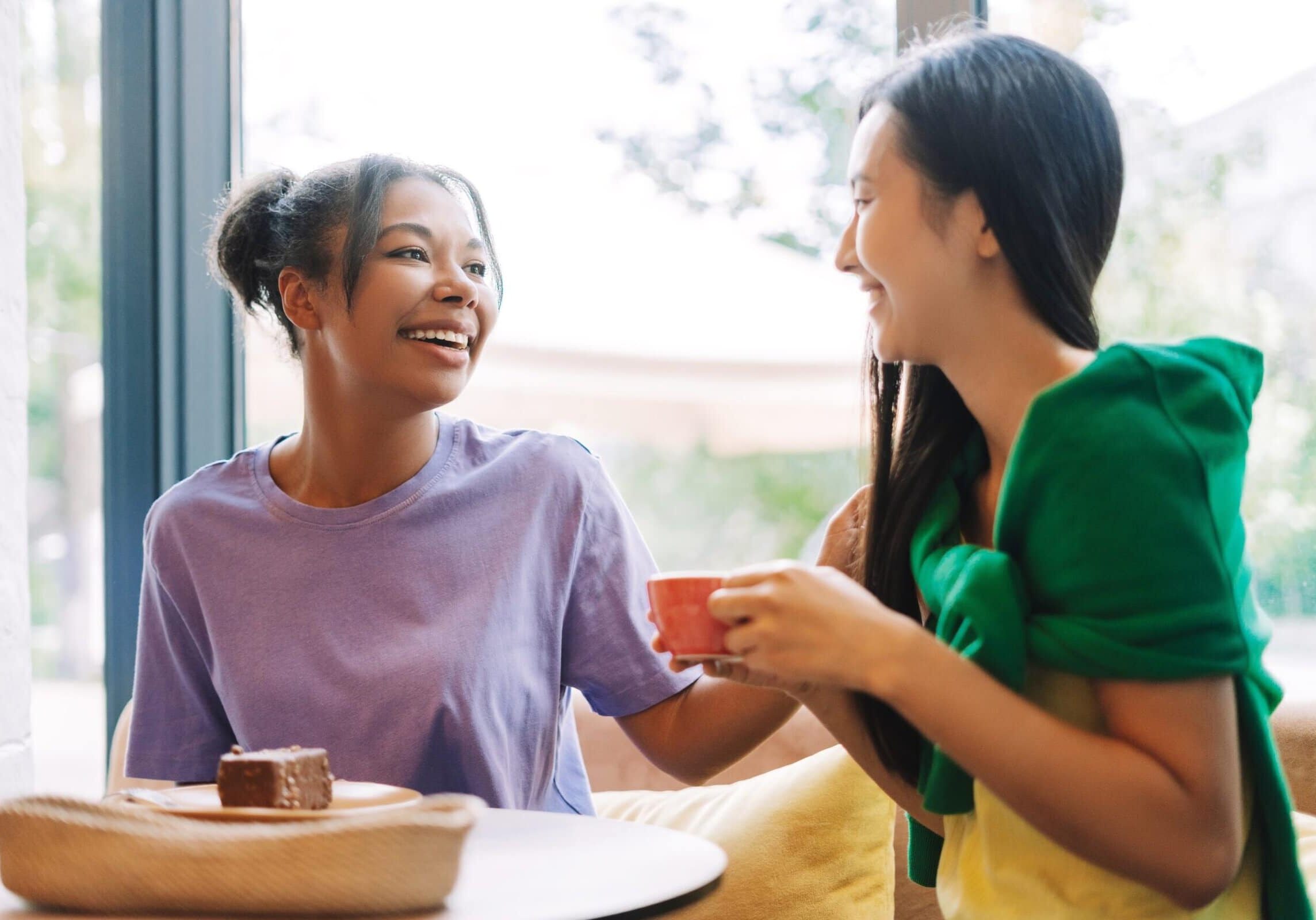 Two friends laughing and talking over coffee at a table