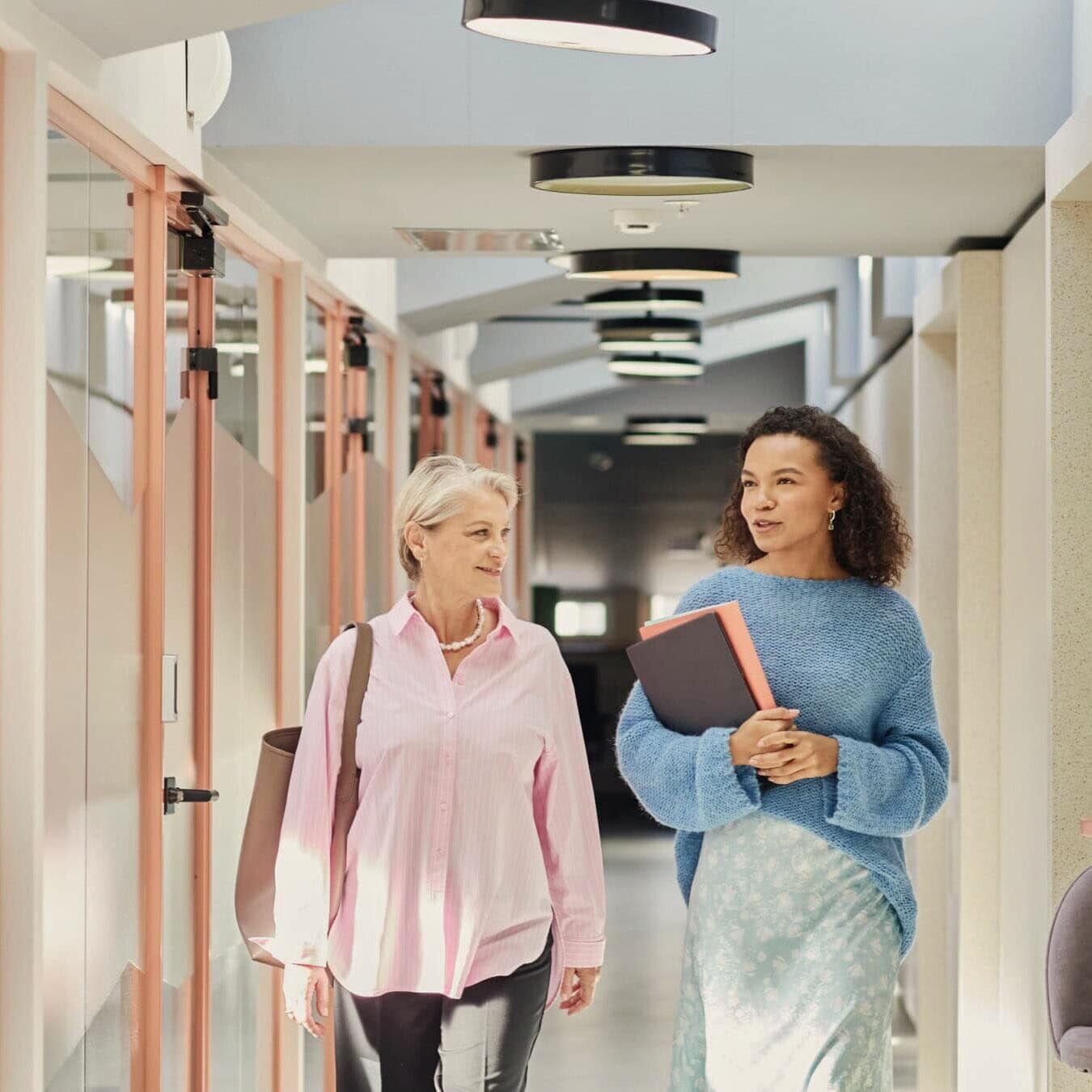 Two woman are walking through an office building talking about the ICF Business Partners