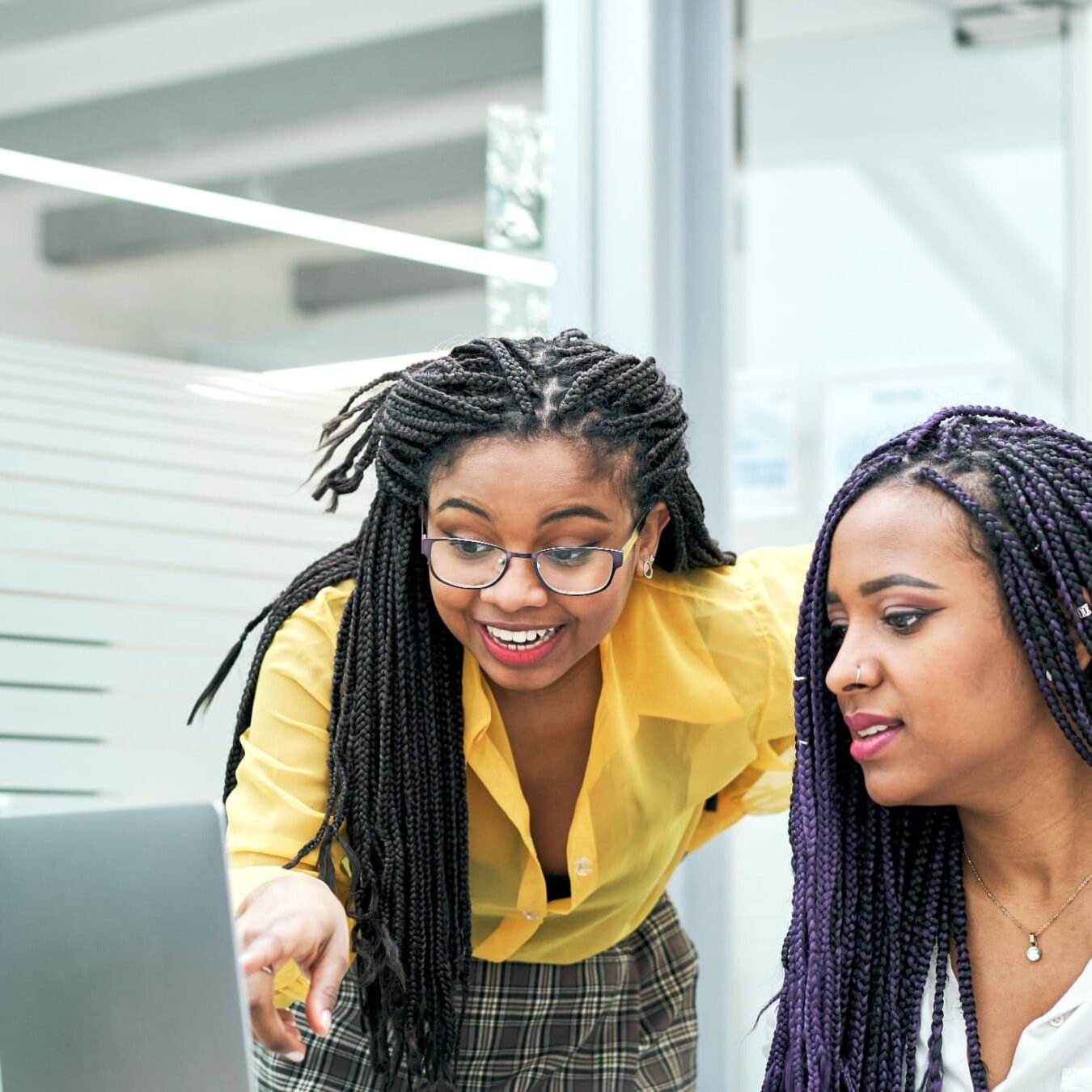 Two women look at a laptop in an office setting