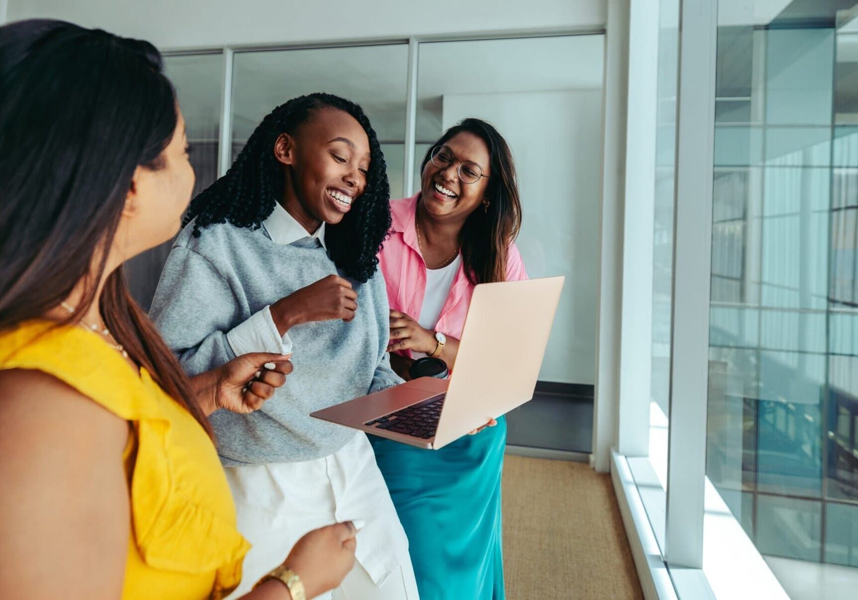 Three coworkers talking and smiling together in a modern office hallway