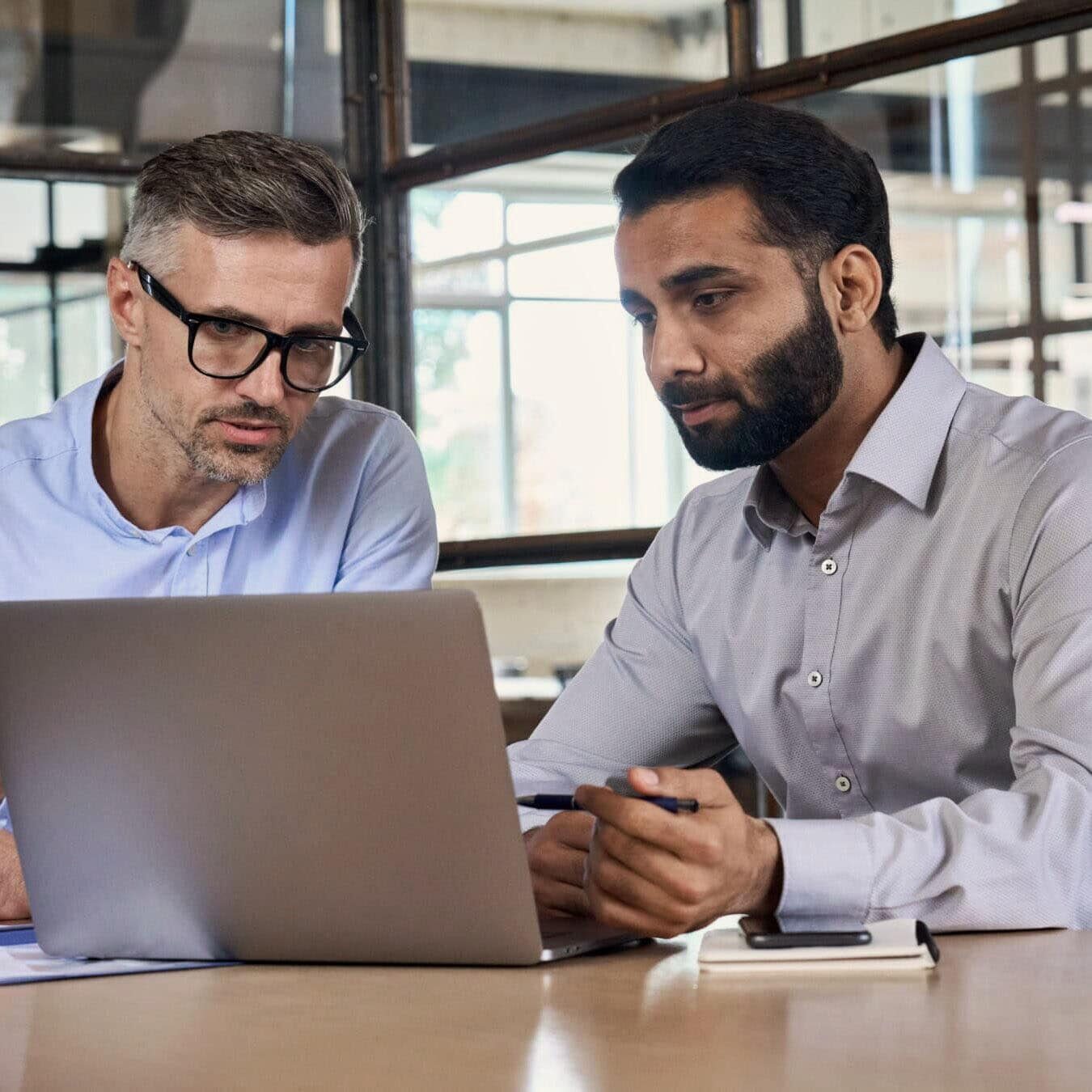 Two men look at a laptop to registration for an exam in a professional office