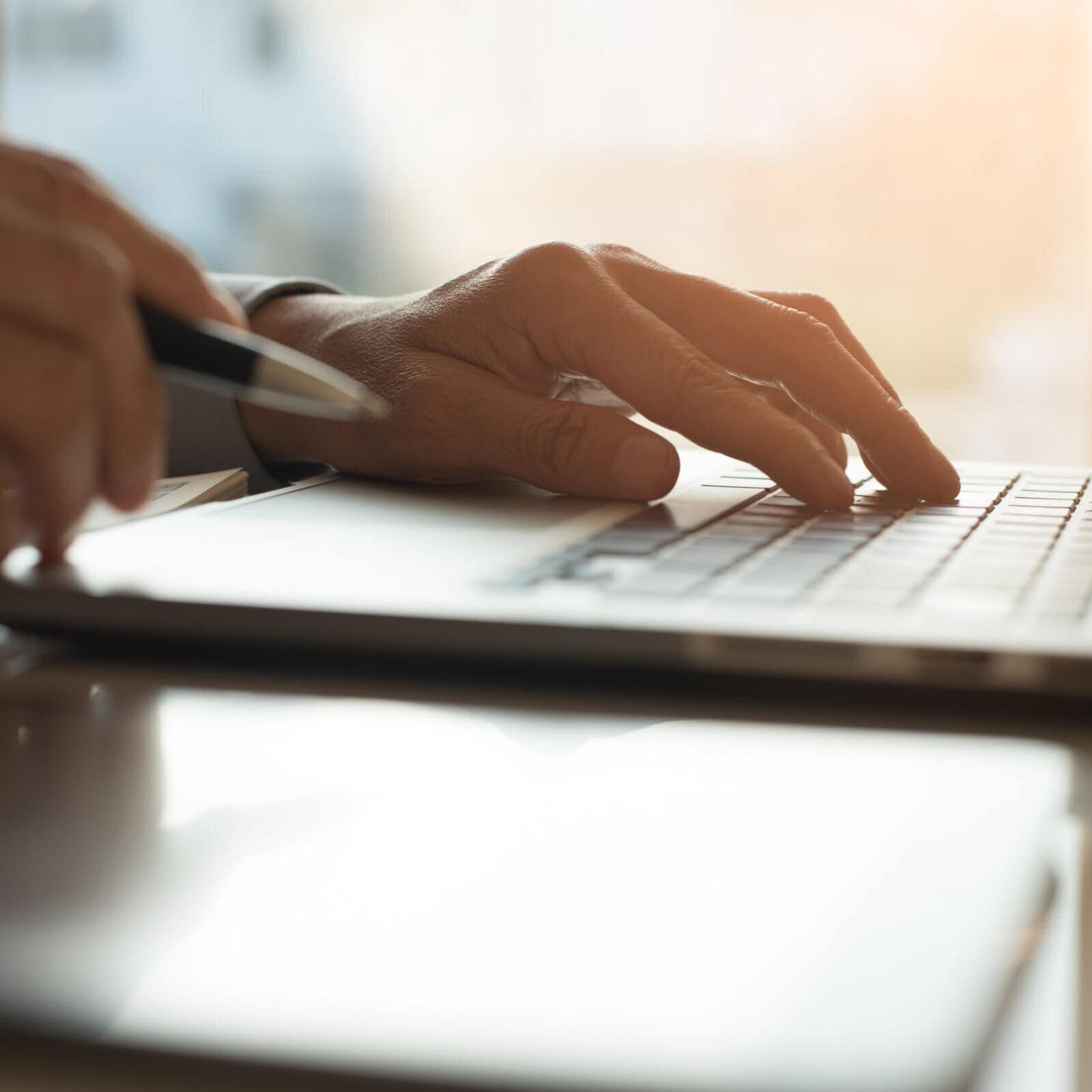 Hands typing on a laptop keyboard while holding a pen at a desk