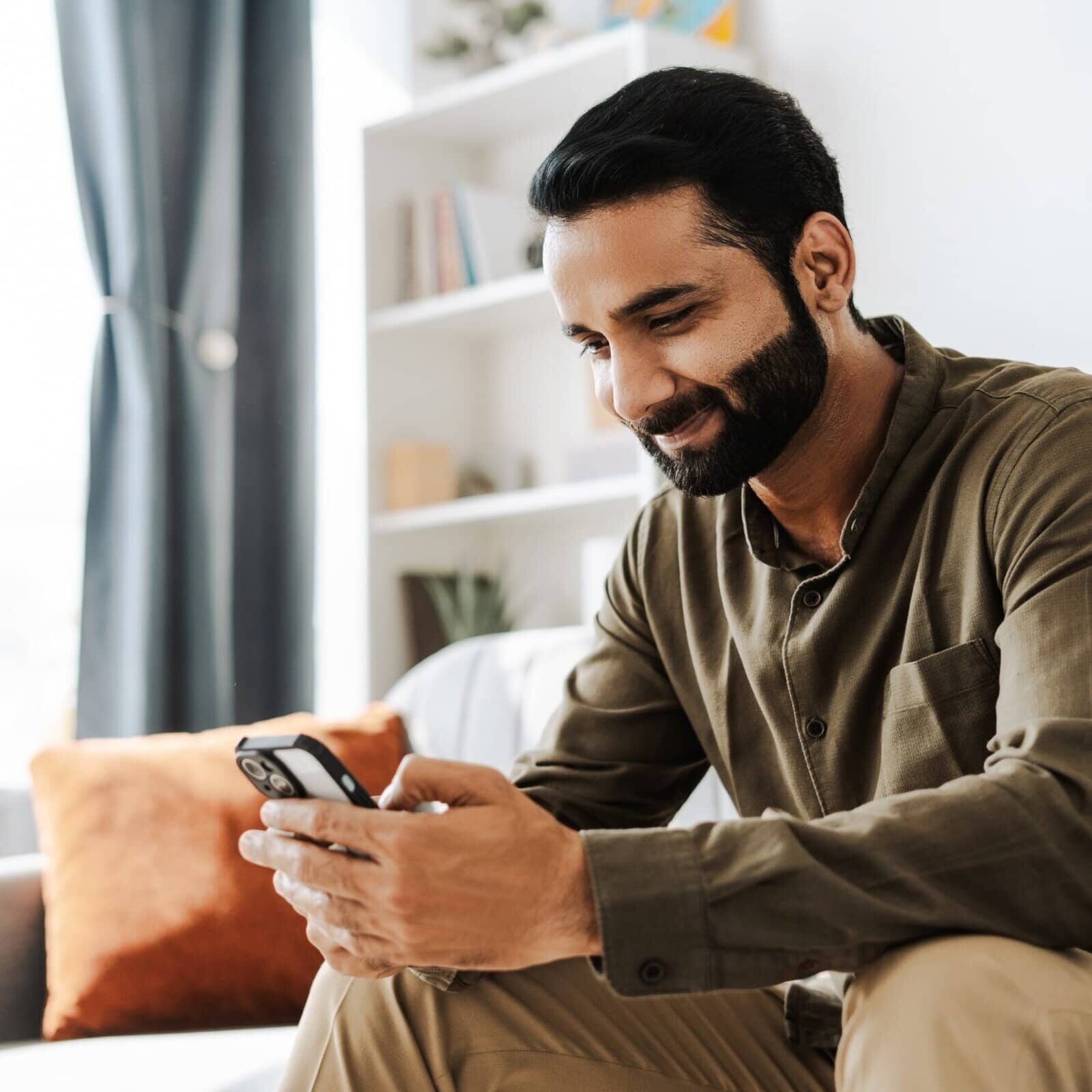 Man sitting on a couch smiling while looking at his smartphone