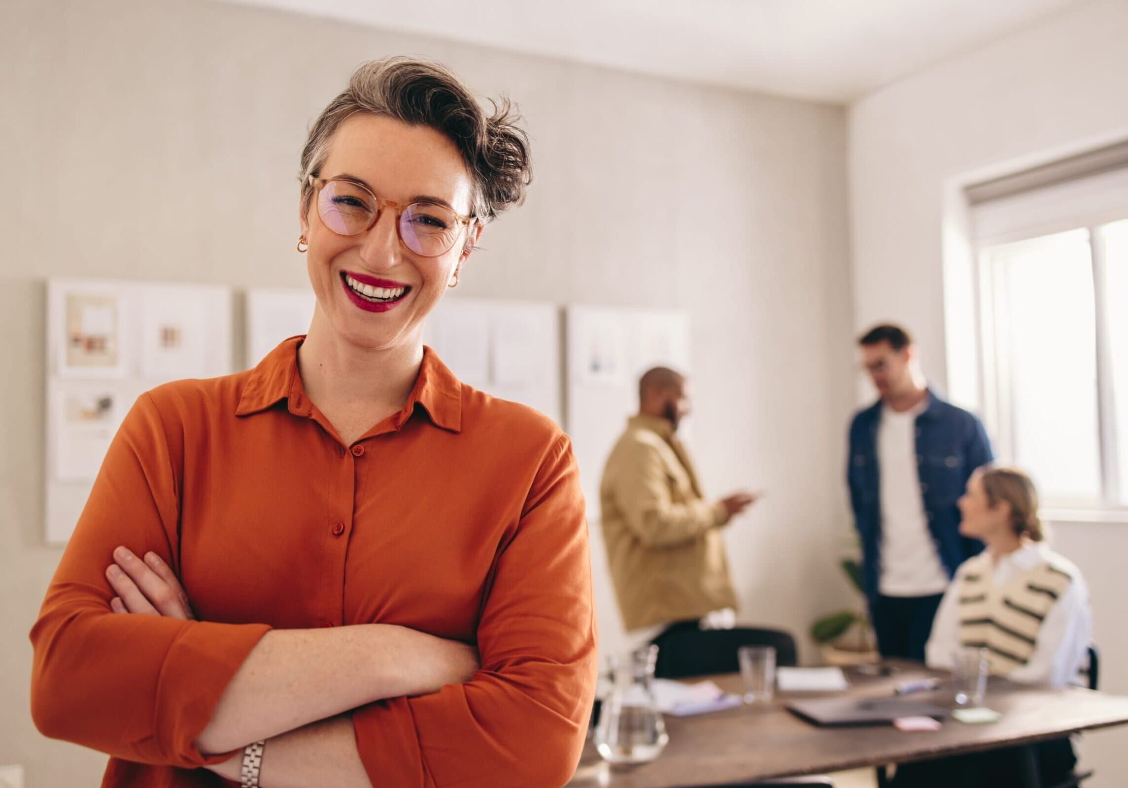 A confident professional smiles at the camera while standing in a well-lit office space.