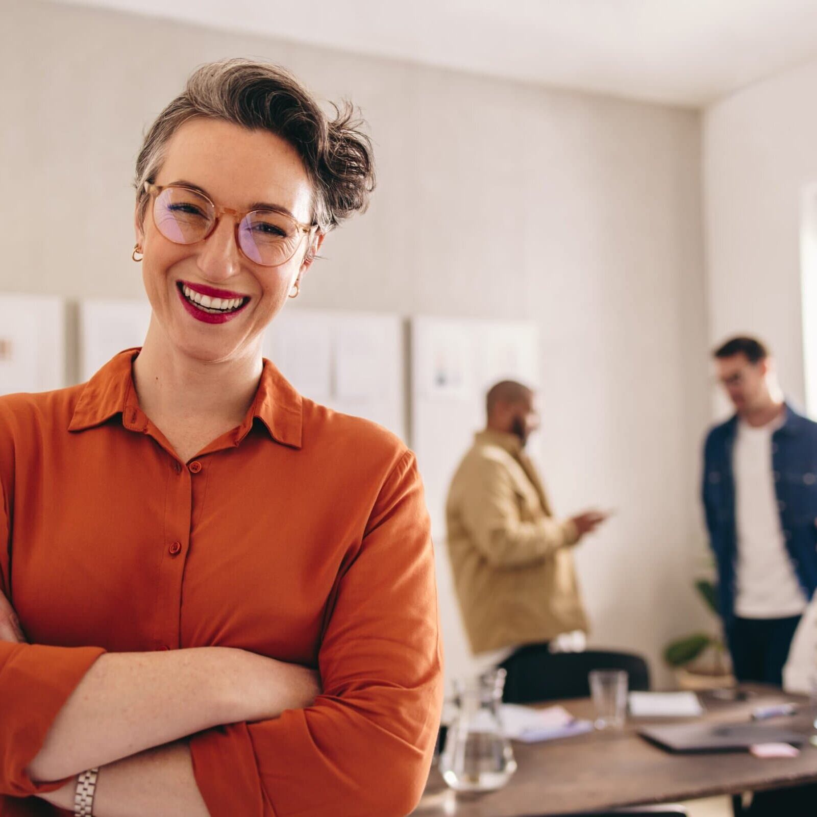 A confident professional smiles at the camera while standing in a well-lit office space.