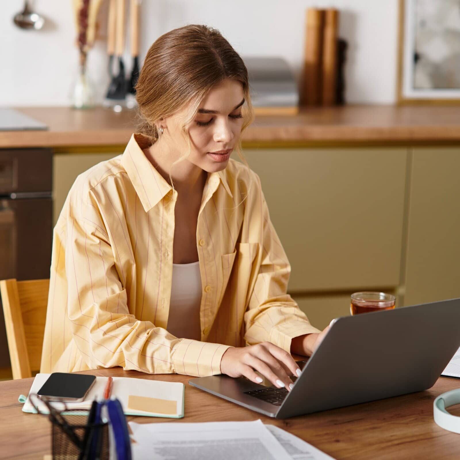 Young woman working on a laptop at a home desk with notebook and coffee