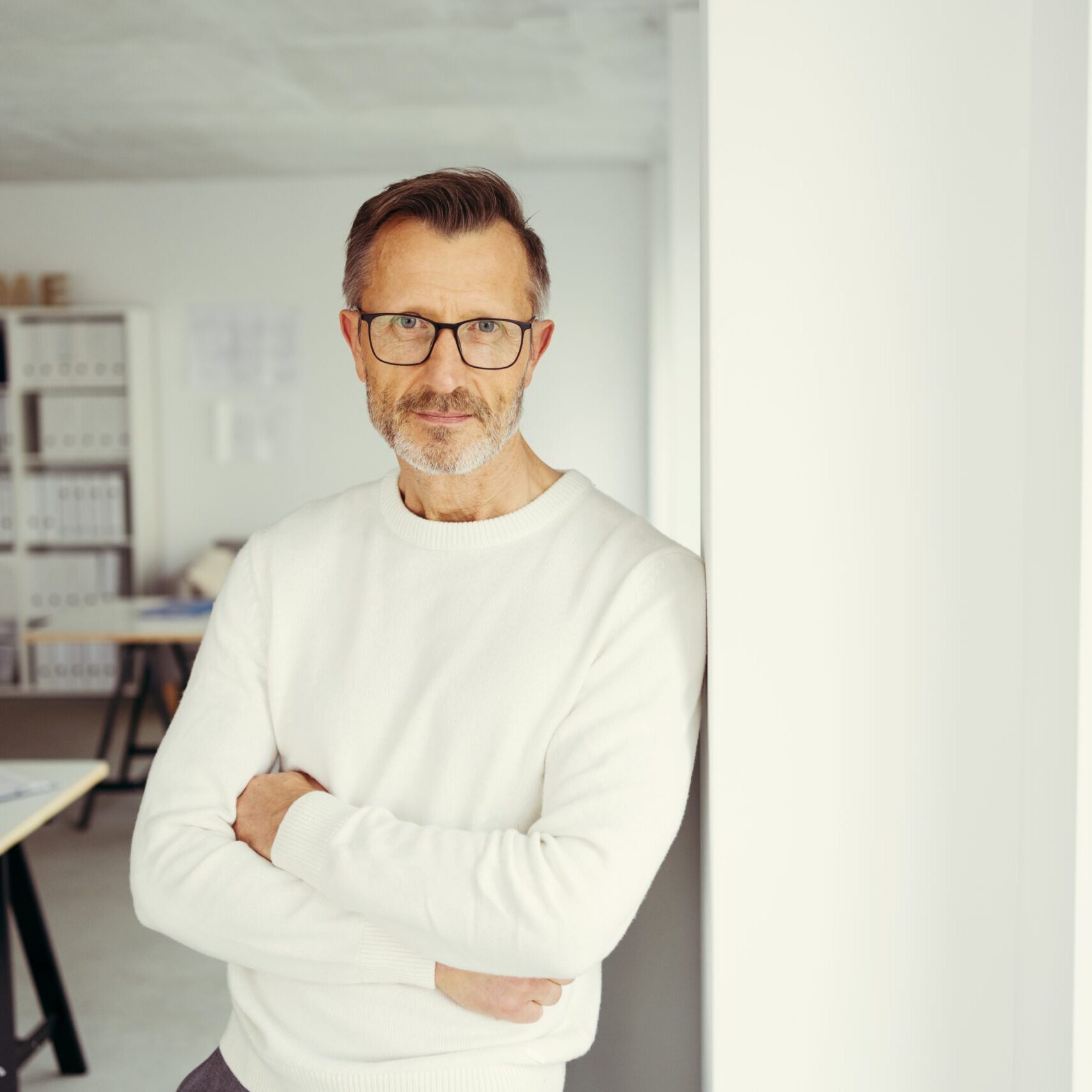 Middle-aged man with glasses standing with arms crossed in a modern office