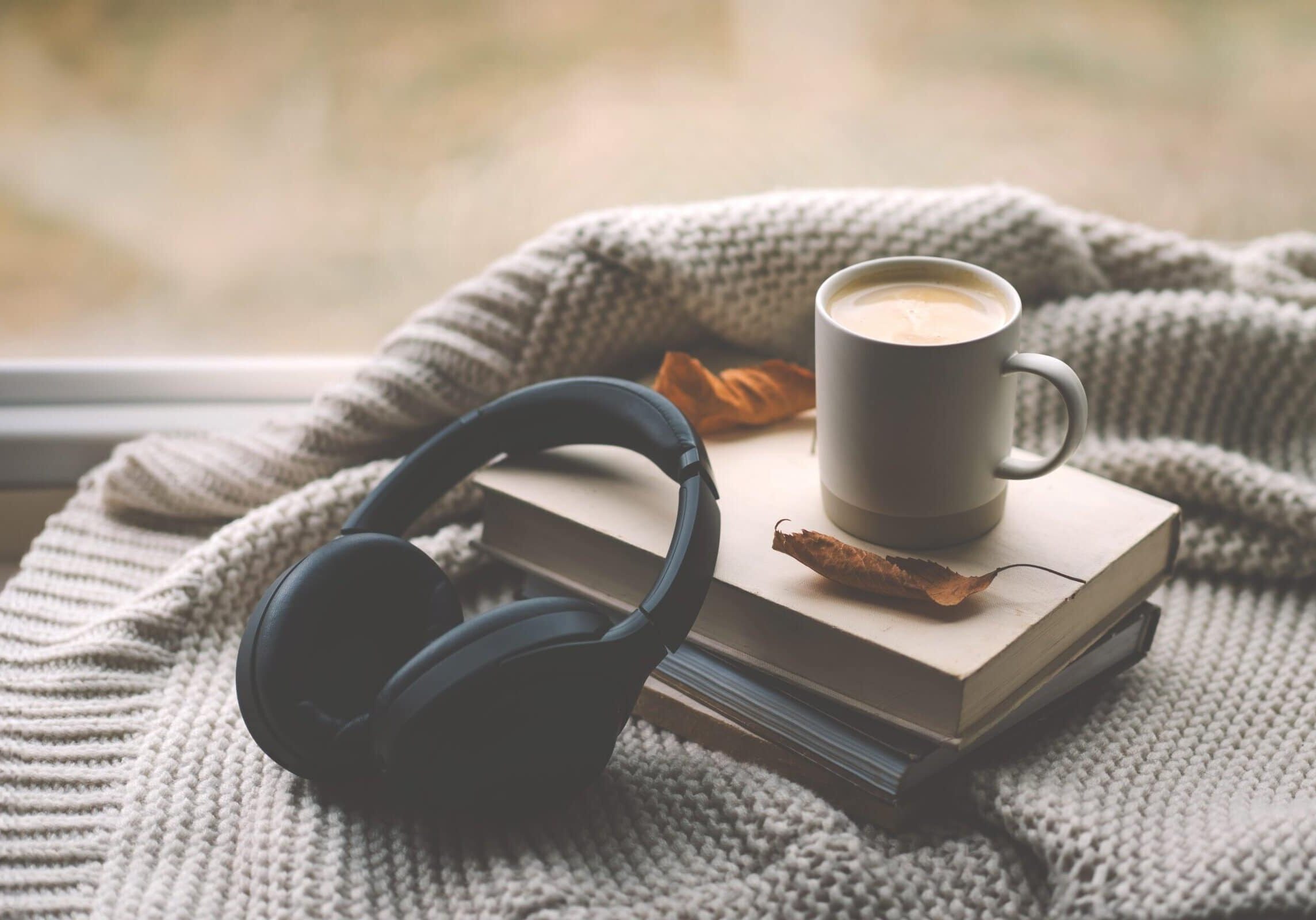 Black headphones placed on a book beside a mug