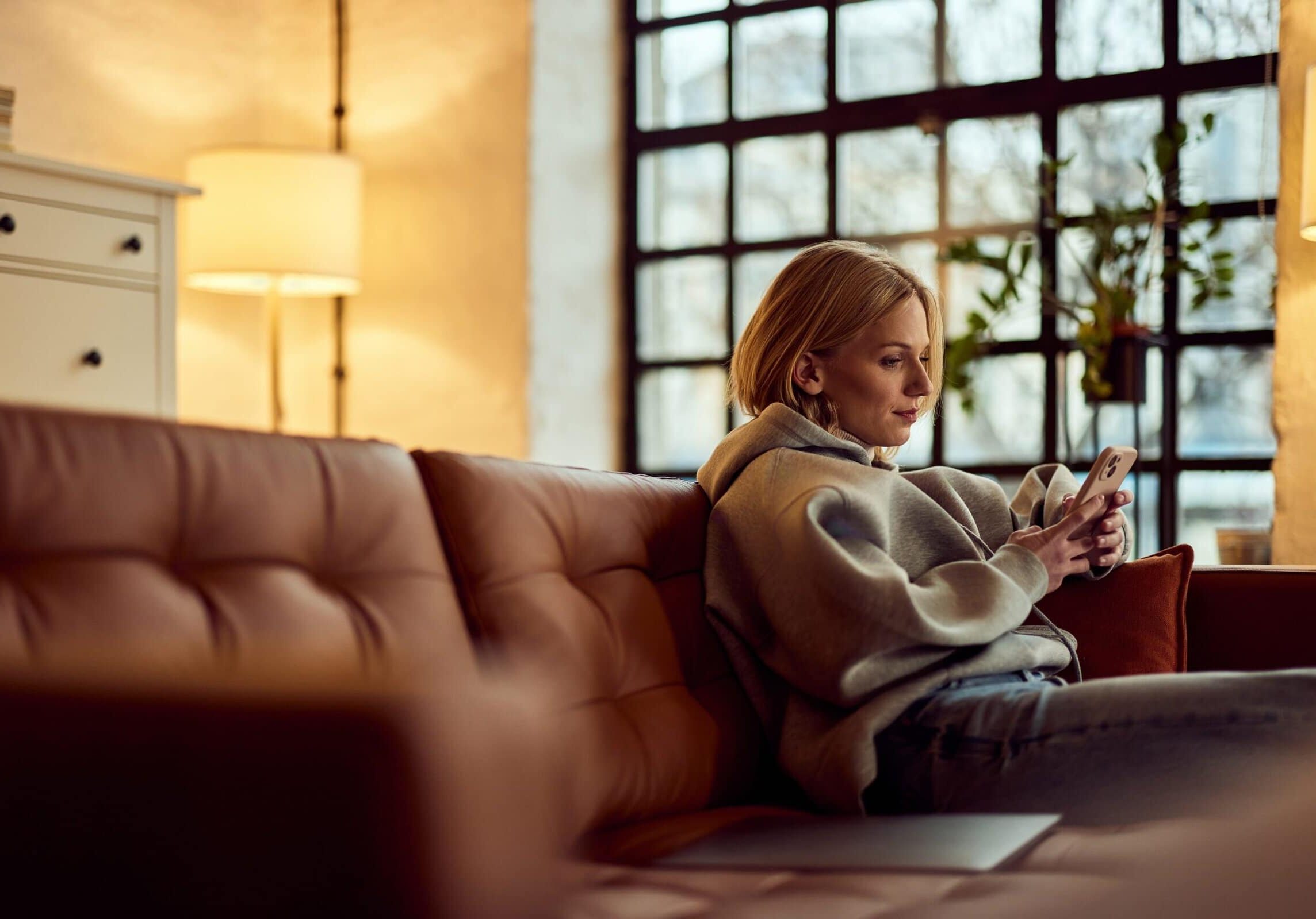 Young woman sitting on a couch indoors using her smartphone in a cozy living room
