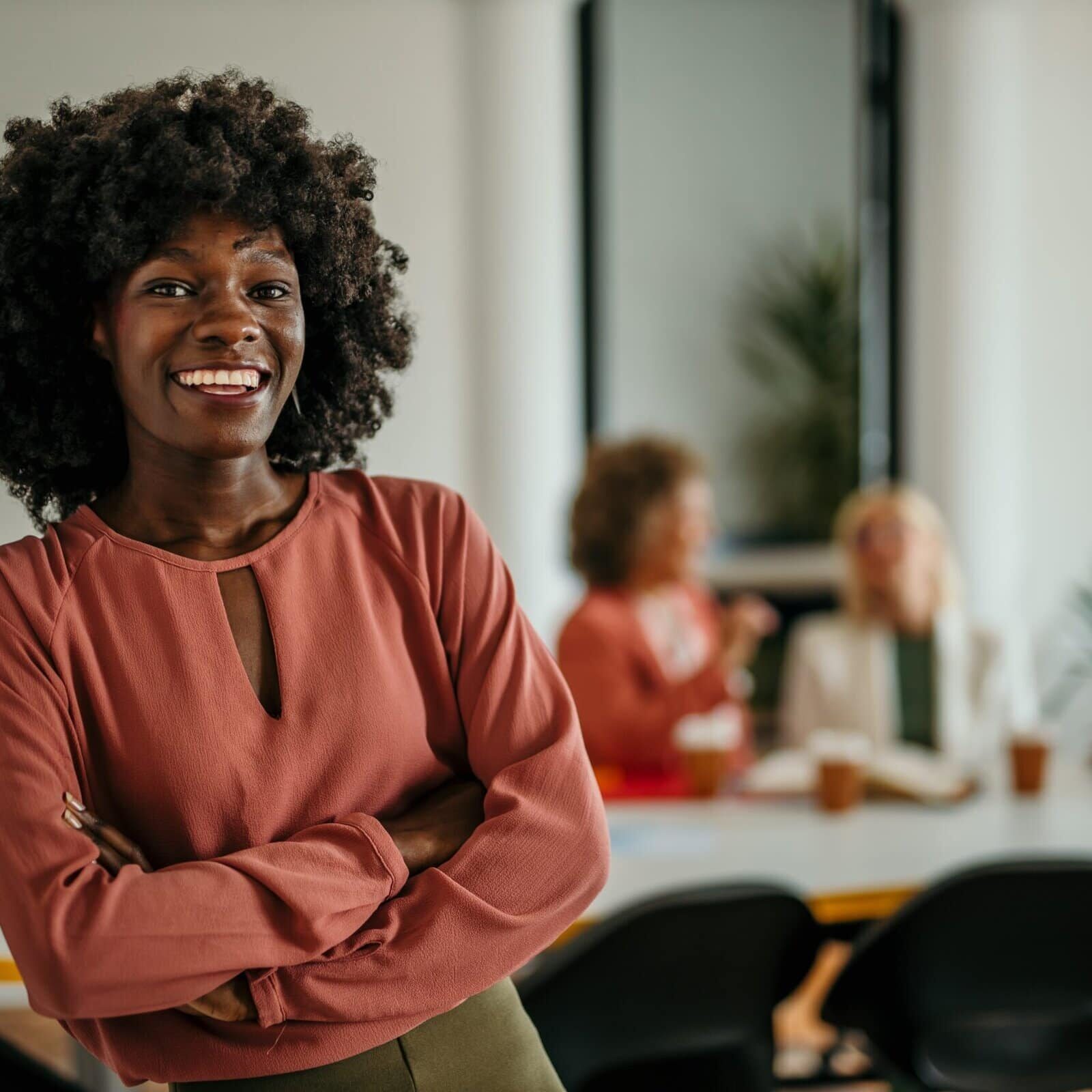 Confident professional standing with arms crossed in front of colleagues meeting in a modern office