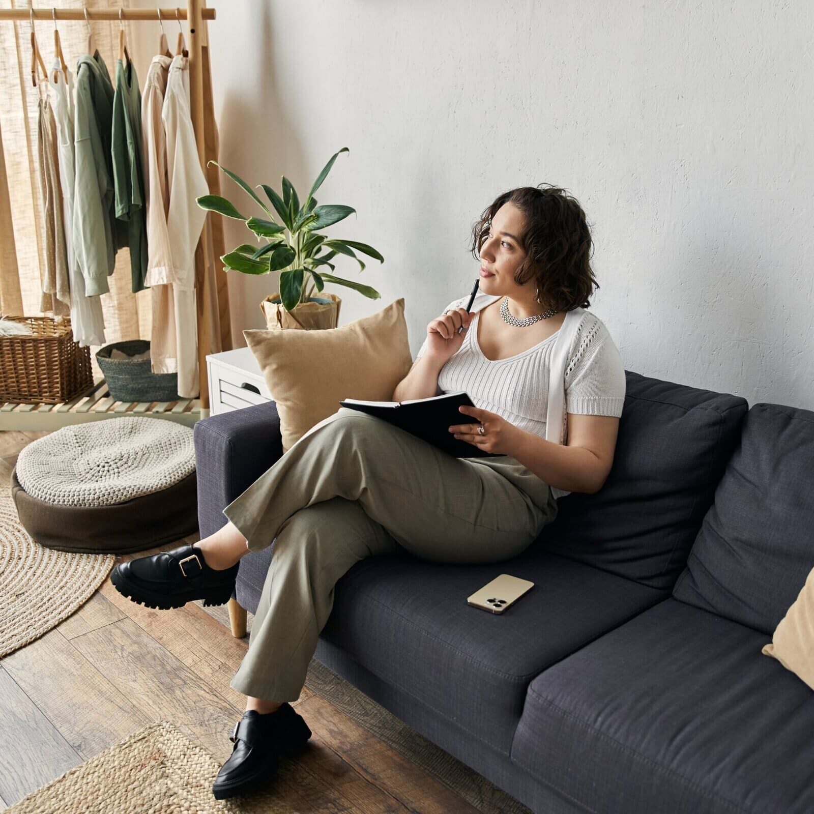 Young woman sitting on a sofa writing in a notebook in a bright living room