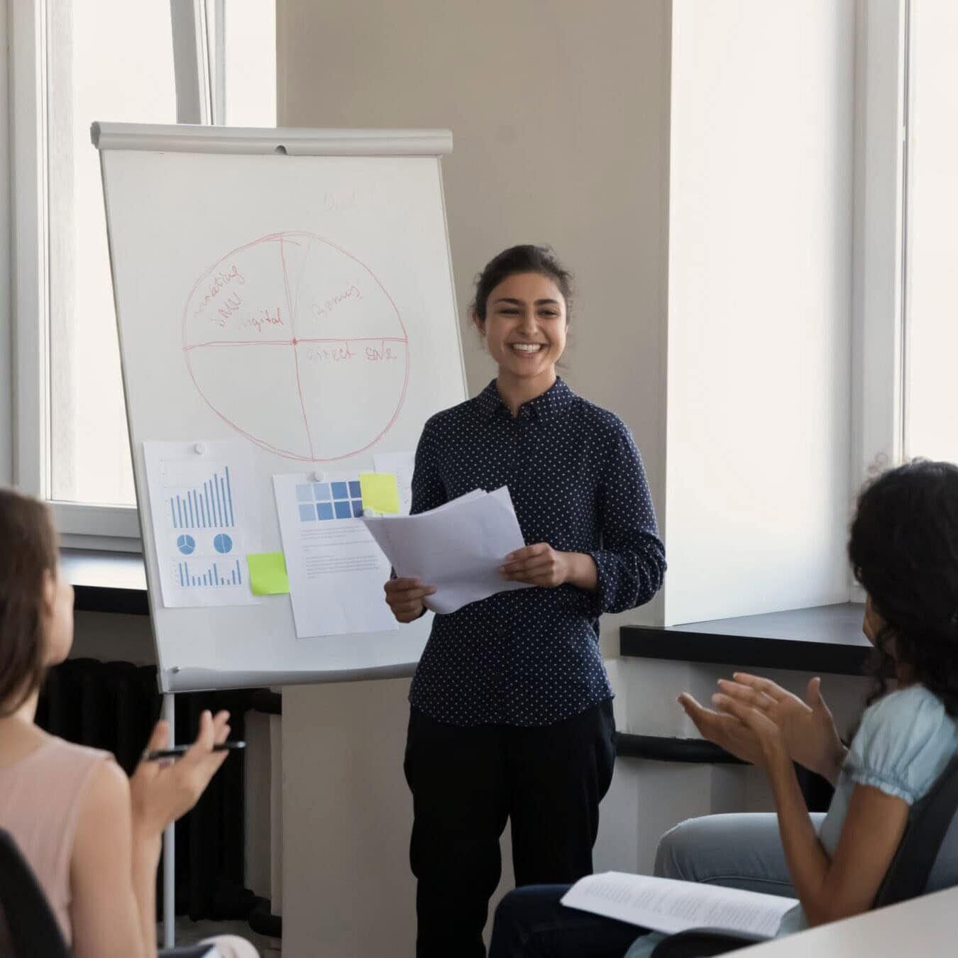 A woman is giving a presentation to a group of people in a casual office.