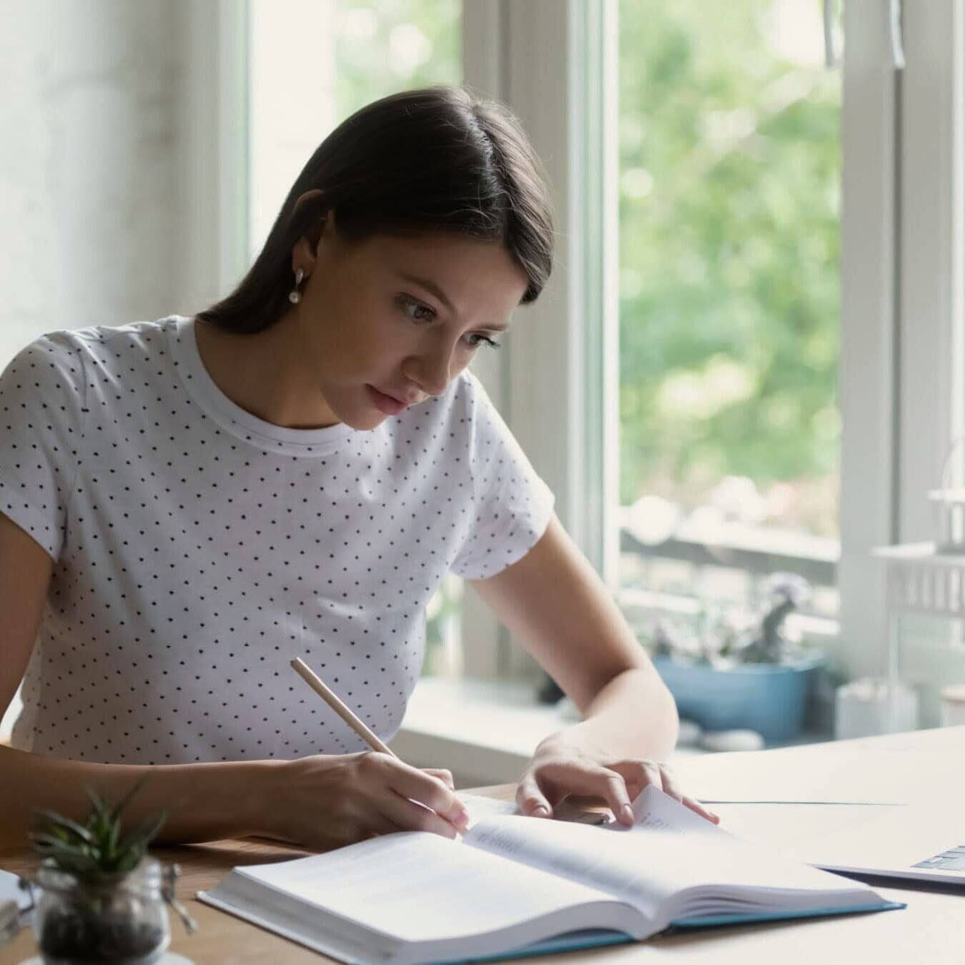 A woman is writing in a notebook at a home office.