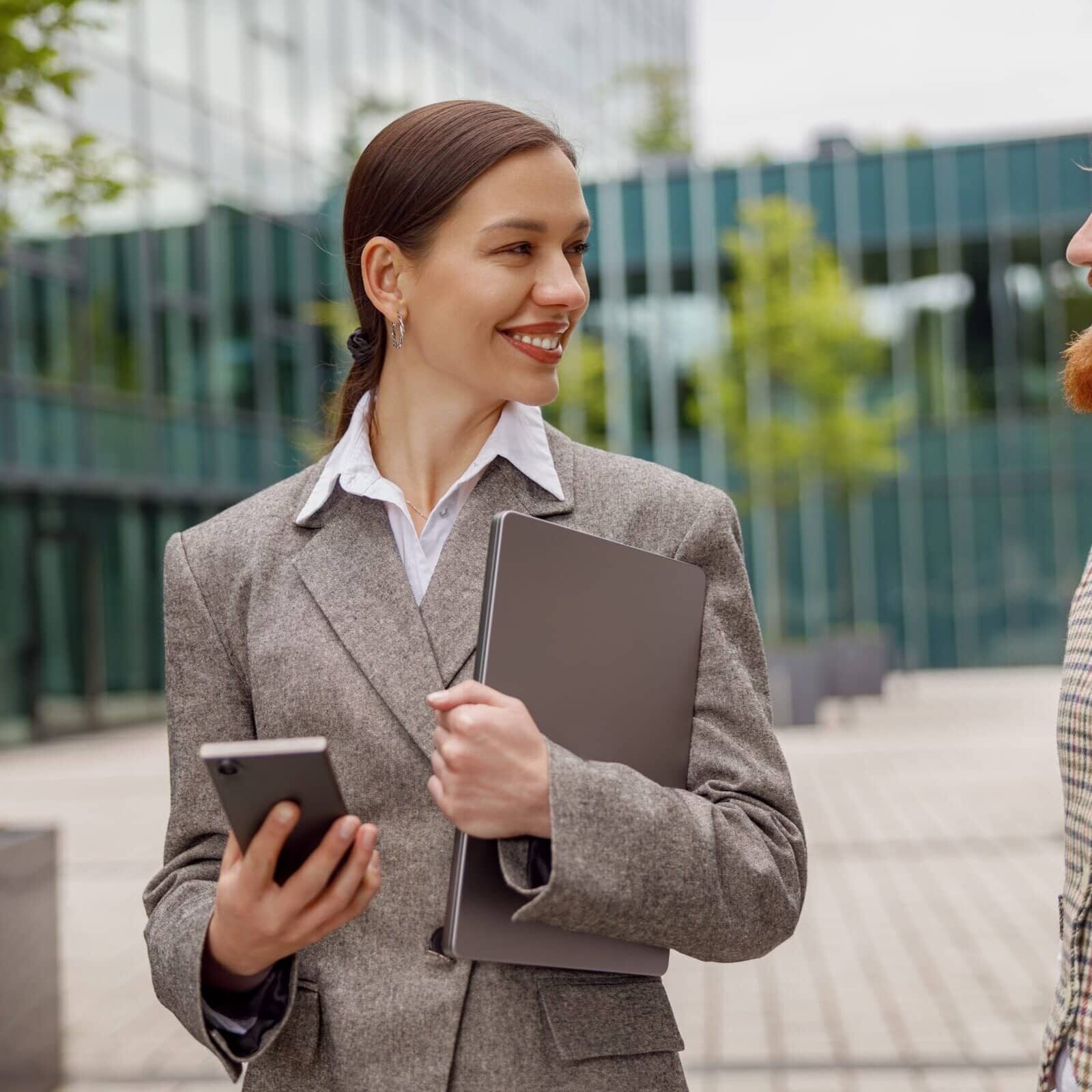 Two professionals in business attire talking outdoors while holding work documents