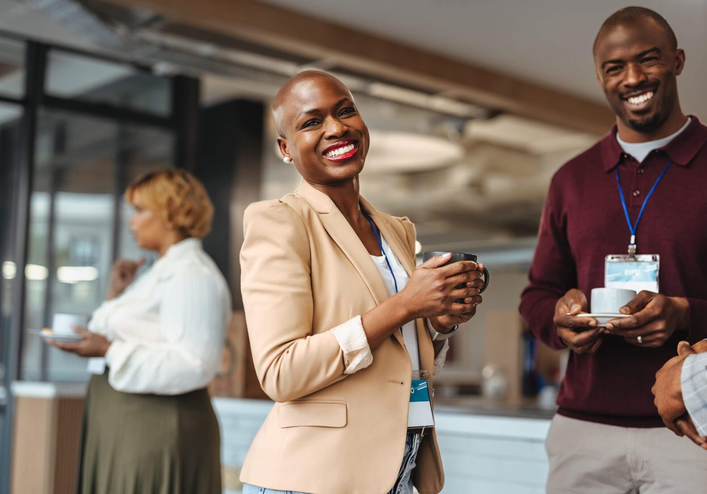 Three colleagues smiling and holding coffee mugs during a casual workplace conversation