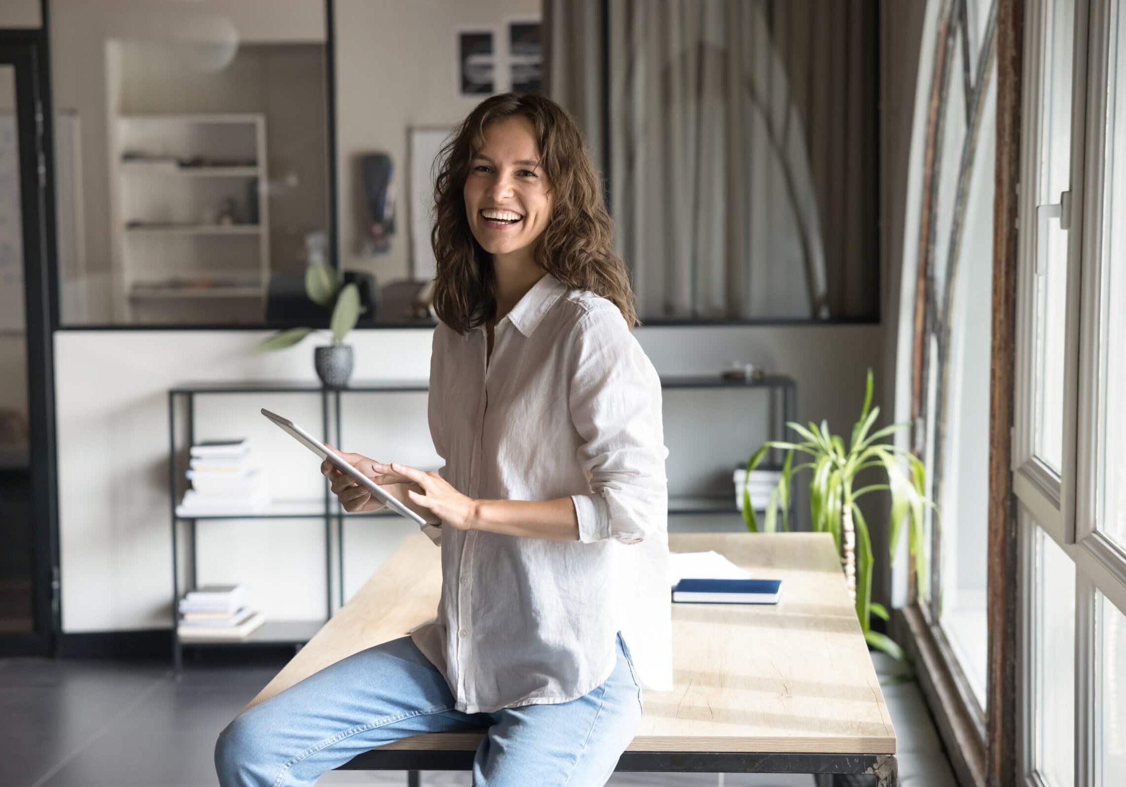 Businesswoman sitting on desk holding tablet in modern office