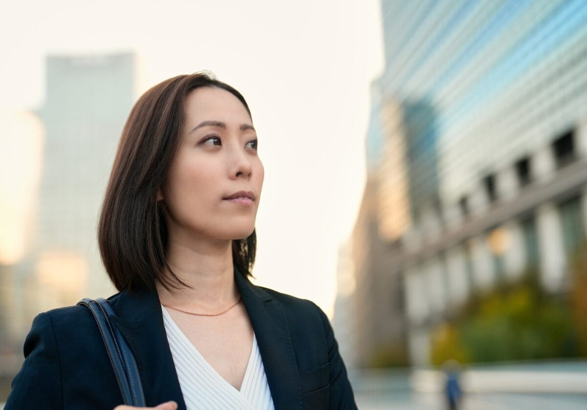 A professional woman in a blazer looking thoughtfully into the distance against a blurred city background.