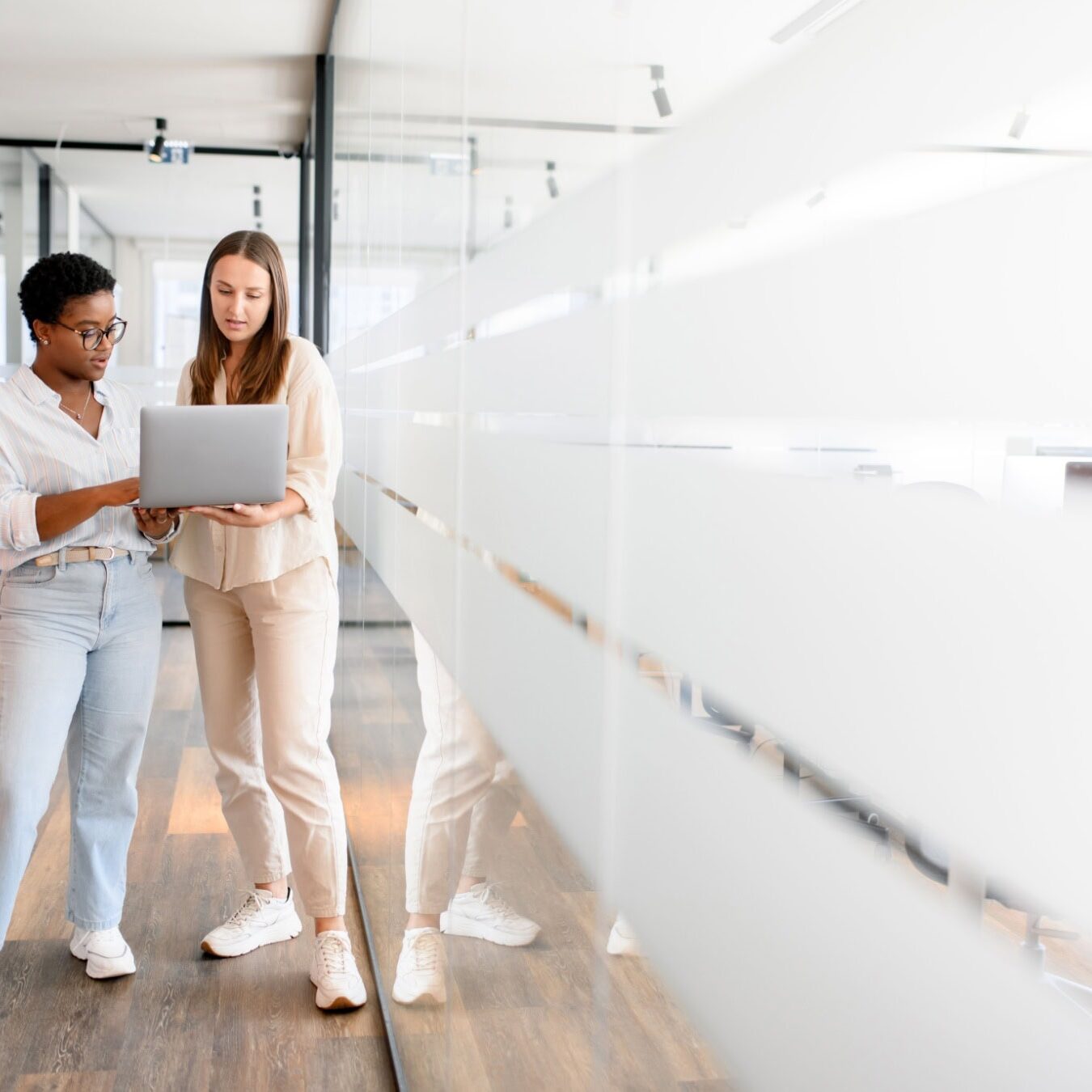 Two women walk through a professional offices halls with a laptop