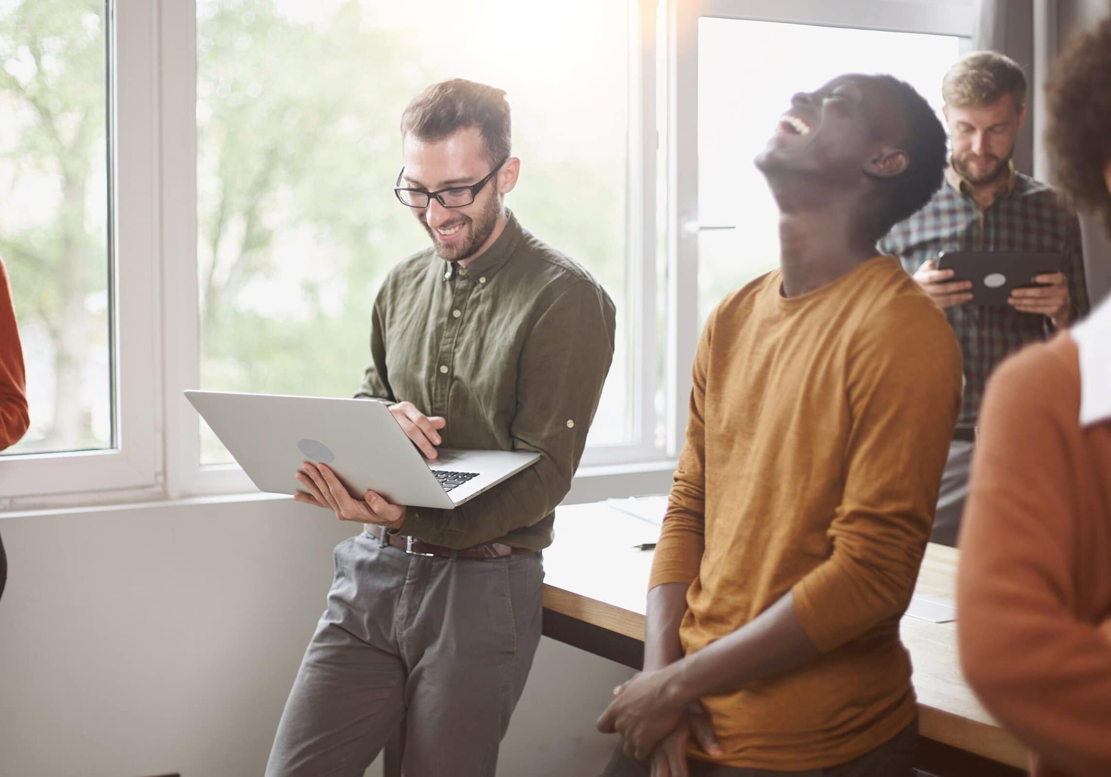 Employees standing near a table in a coworking space while reviewing work on a laptop and talking