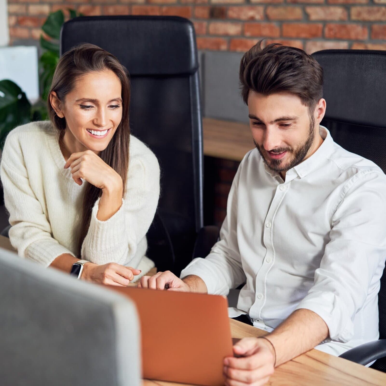 Two young business professionals talking and looking at a laptop in a modern office