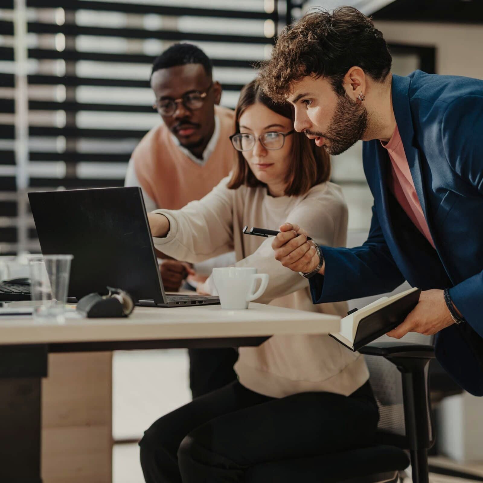 three people at a laptop with one pointing to something on a laptop screen