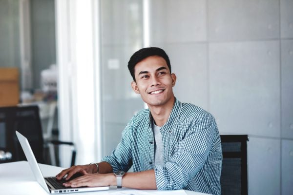 man smiling while working on a laptop and looking to his left